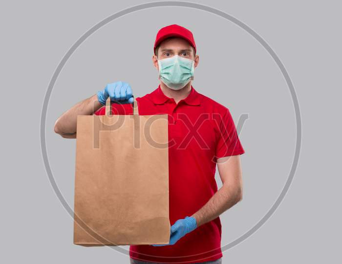 Delivery Man Wearing Medical Mask And Gloves With Paper Bag In Hands. Red Uniform Delivery Boy. Home Food Delivery. Paper Bag