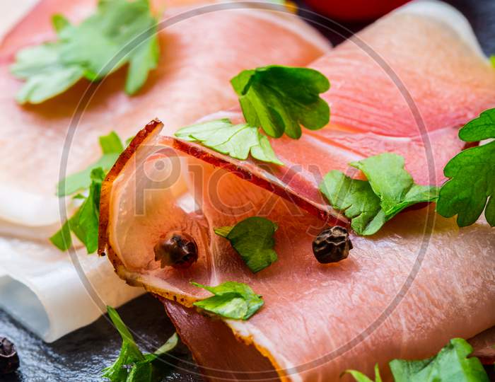 Prosciutto. Curled Slices of Delicious Prosciutto with parsley leaves on granite board. Prosciuto with spice cherry tomatoes garlic and olive. Italian and Mediterranean cuisine