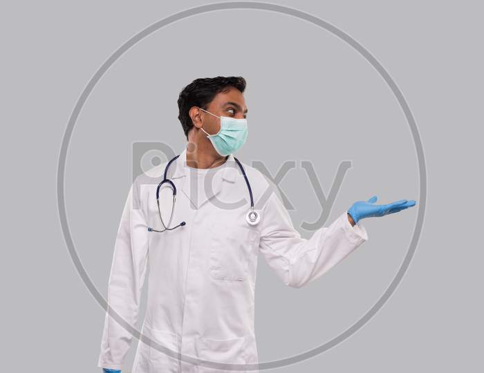 Doctor Holding Hand To Side Wearing Medical Mask And Gloves Watching To Side Isolated. Indian Man Doctor Sign