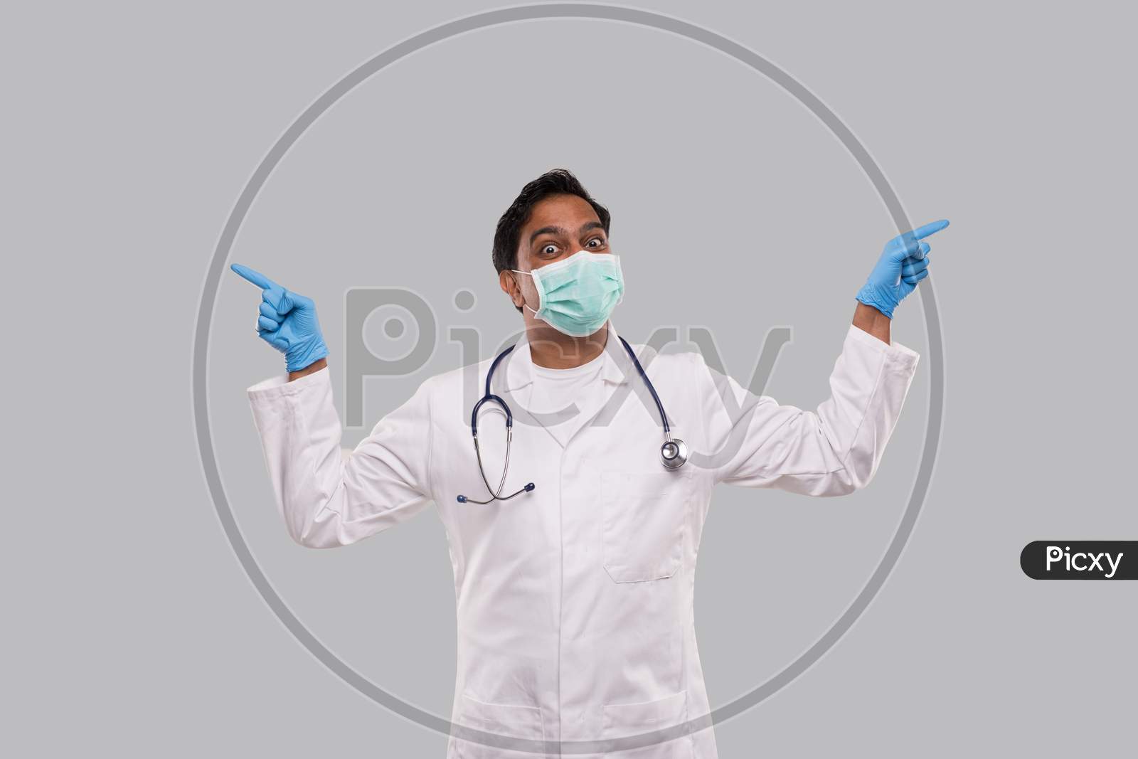 Indian Man Doctor Pointing To Sides Both Hands Wearing Medical Mask And Gloves. Isolated