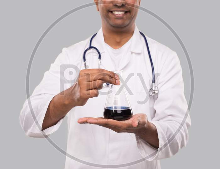 Male Doctor Showing Flask With Colorfull Liquid Isolated Close Up. Science, Medical, Virus Concept. Indian Man Doctor Smilling.