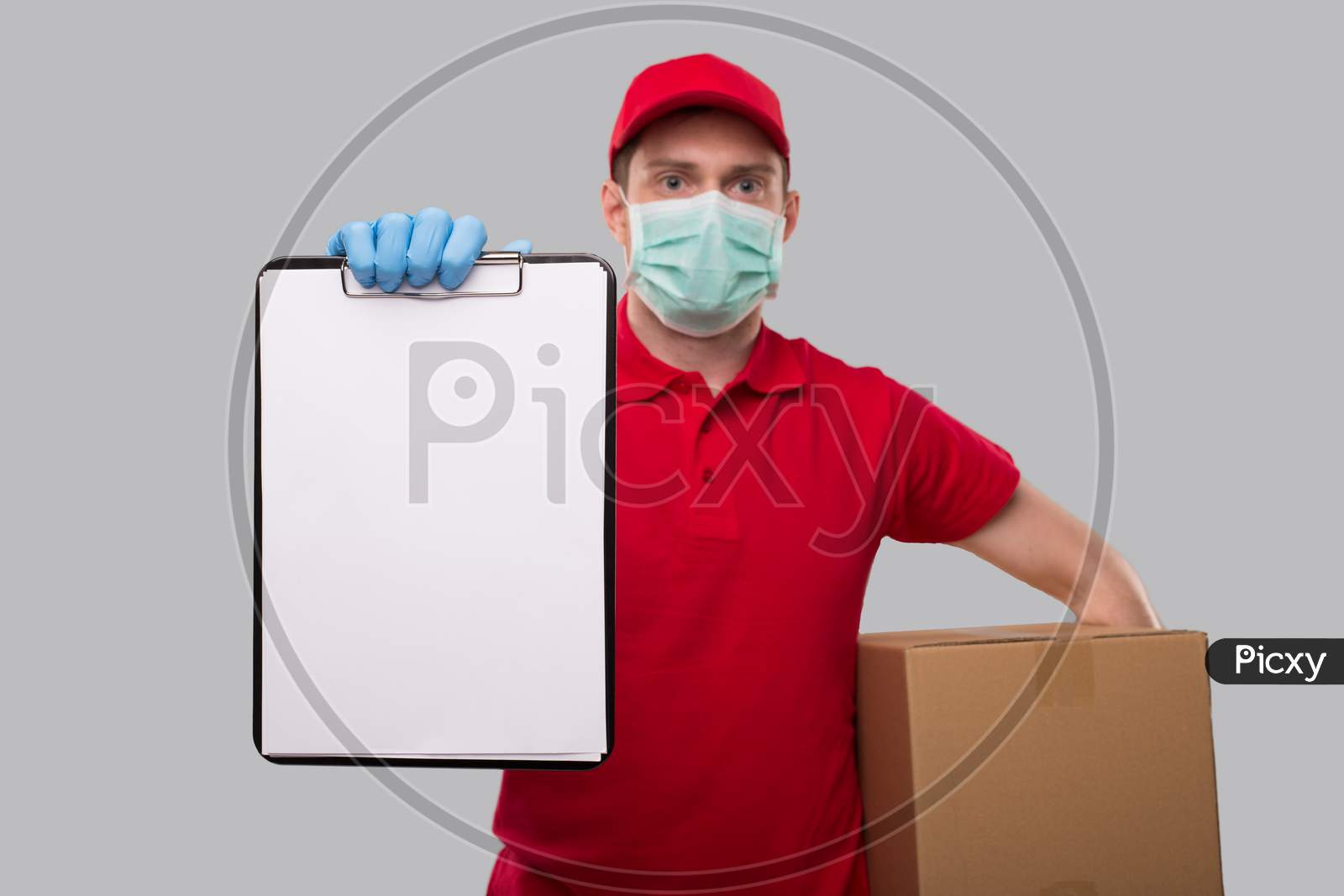 Delivery Man Wearing Medical Mask And Gloves Holding Clipboard And Box In Hands. Blank Clipboard In Hands