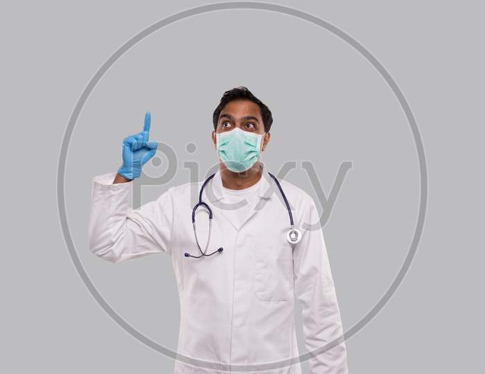 Indian Man Doctor Pointing Up And Watching Up Wearing Medical Mask And Gloves Isolated