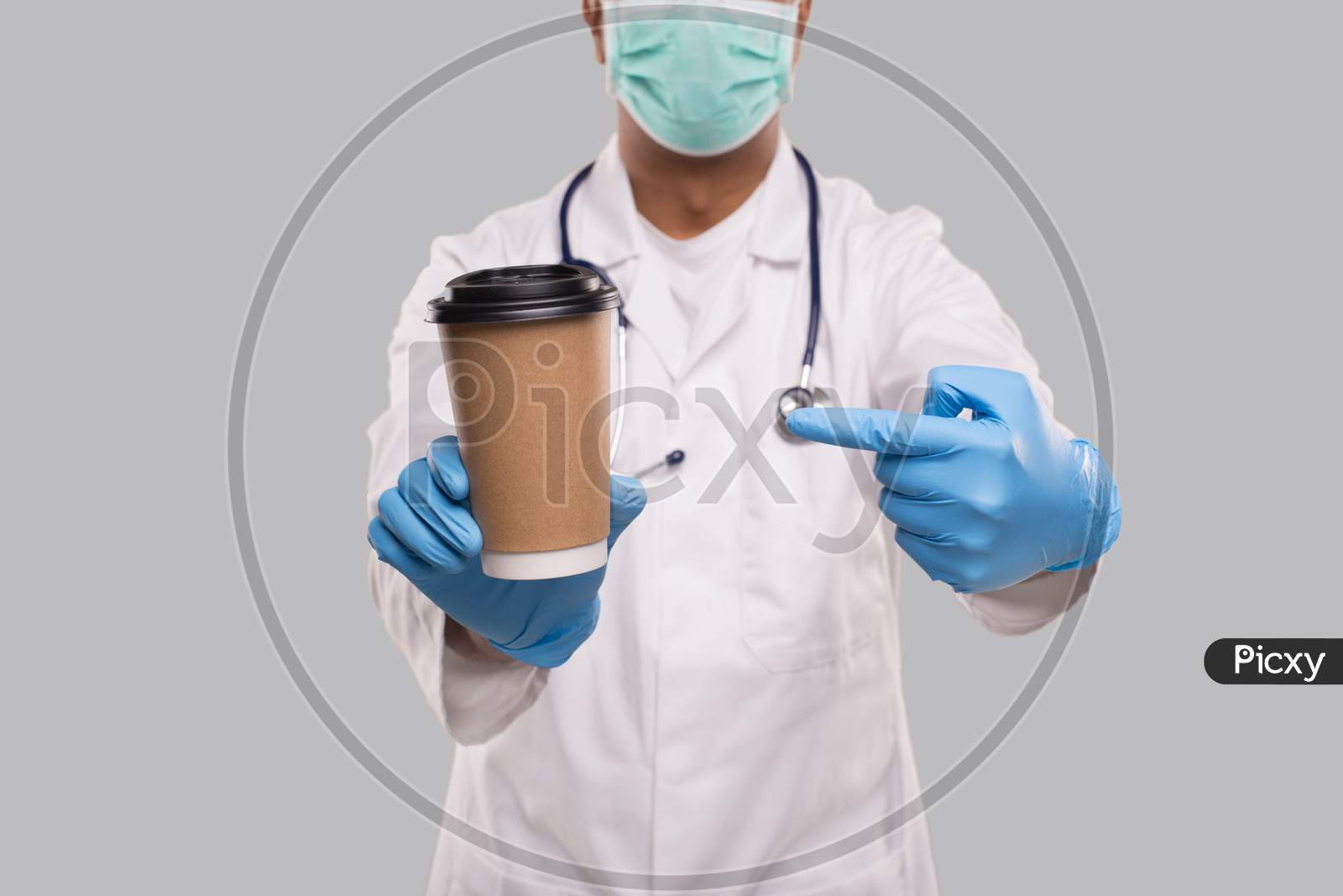 Indian Man Doctor Pointing At Coffee Take Away Cup Wearing Medical Mask And Gloves Close Up Isolated. Indian Doctor Holding Coffee To Go Cup.