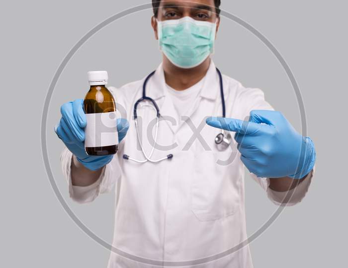 Indian Man Doctor Pointing At Cough Syrup Wearing Medical Mask And Gloves. Hands Wash Antiseptic. Corona Virus Concept. Isolated