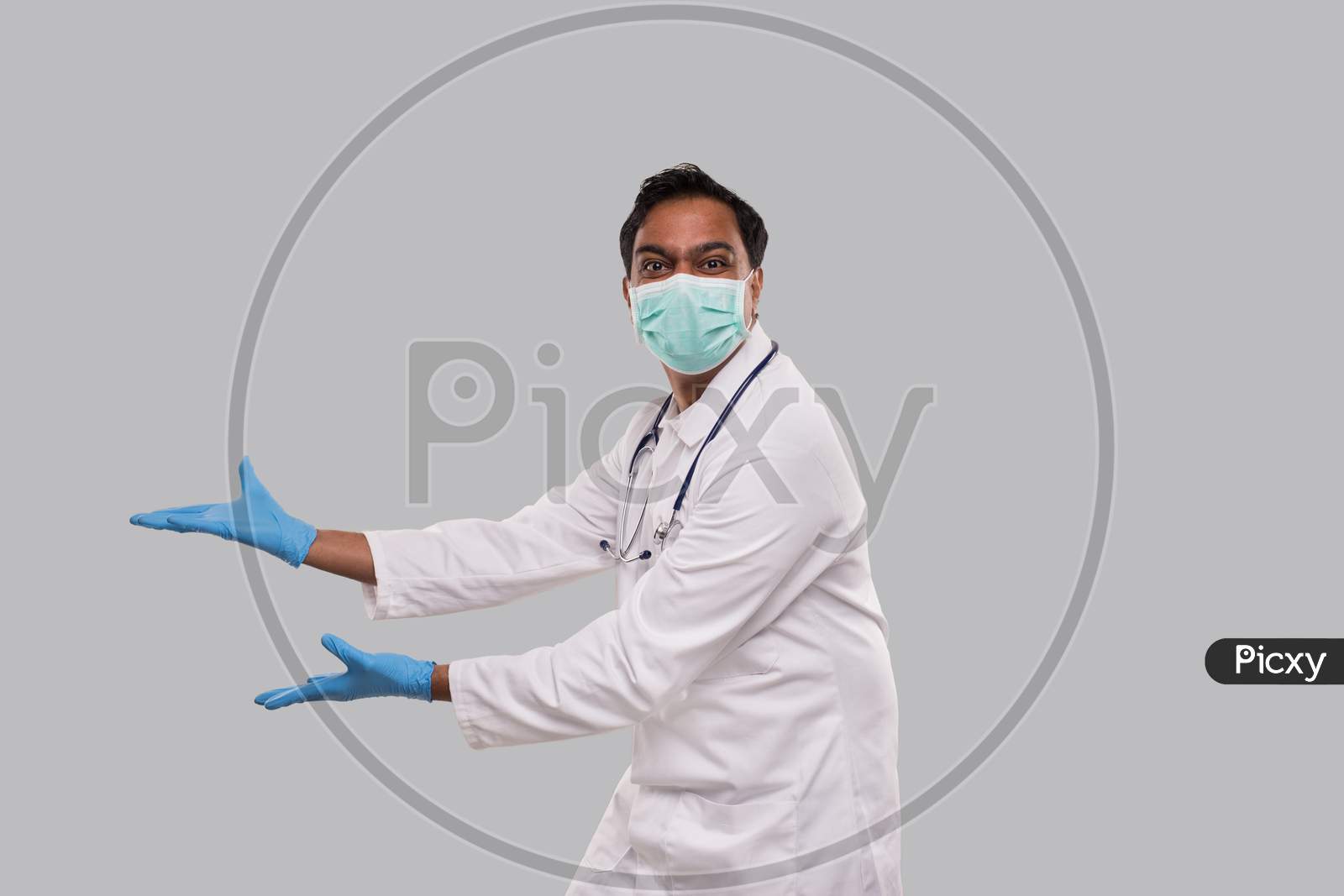 Doctor Holding Open Hands To Side Wearing Medical Mask And Gloves Watching To Camera Isolated. Indian Man Doctor Excited Sign