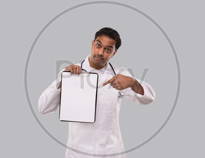 Doctor Pointing At Clipboard Isolated. Indian Man Doctor Blank Clipboard In Hands