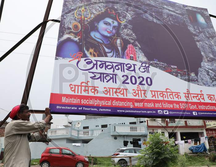 A labourer installs a hoarding outside Yatri Niwas Bhagwati Nagar ahead of the Amarnath Yatra 2020 in Jammu on July 19, 2020