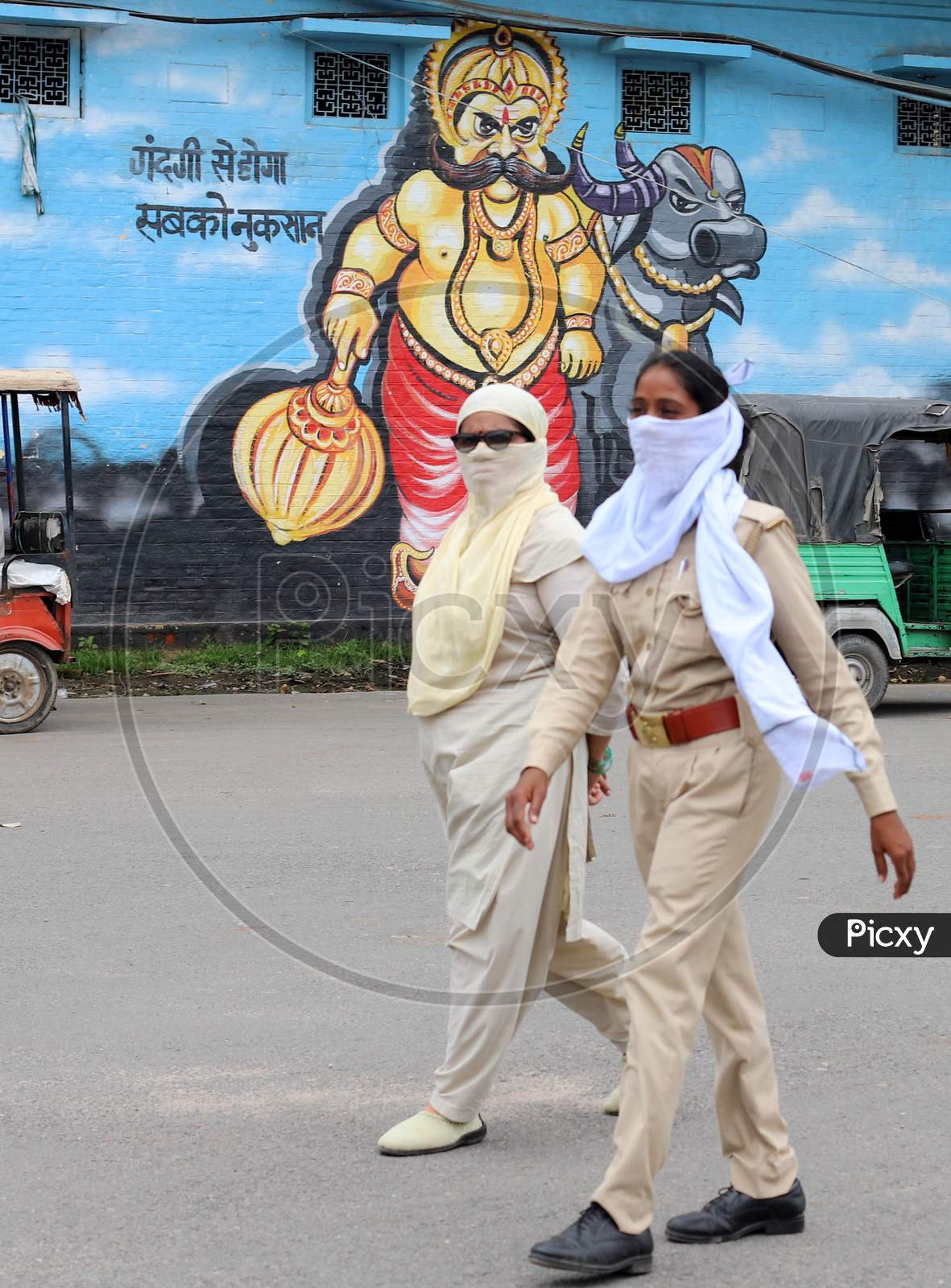 Two women police officers walk in front of a wall which has a mural painting on it during the lockdown in Prayagraj on July 19, 2020