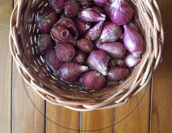 Shallots In A Wicker Basket With A Brown Wooden Base