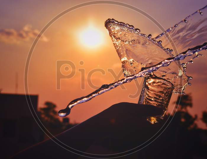 Water Splash Image Of Water Being Thrown Out Of A Glass In Evening Sunset
