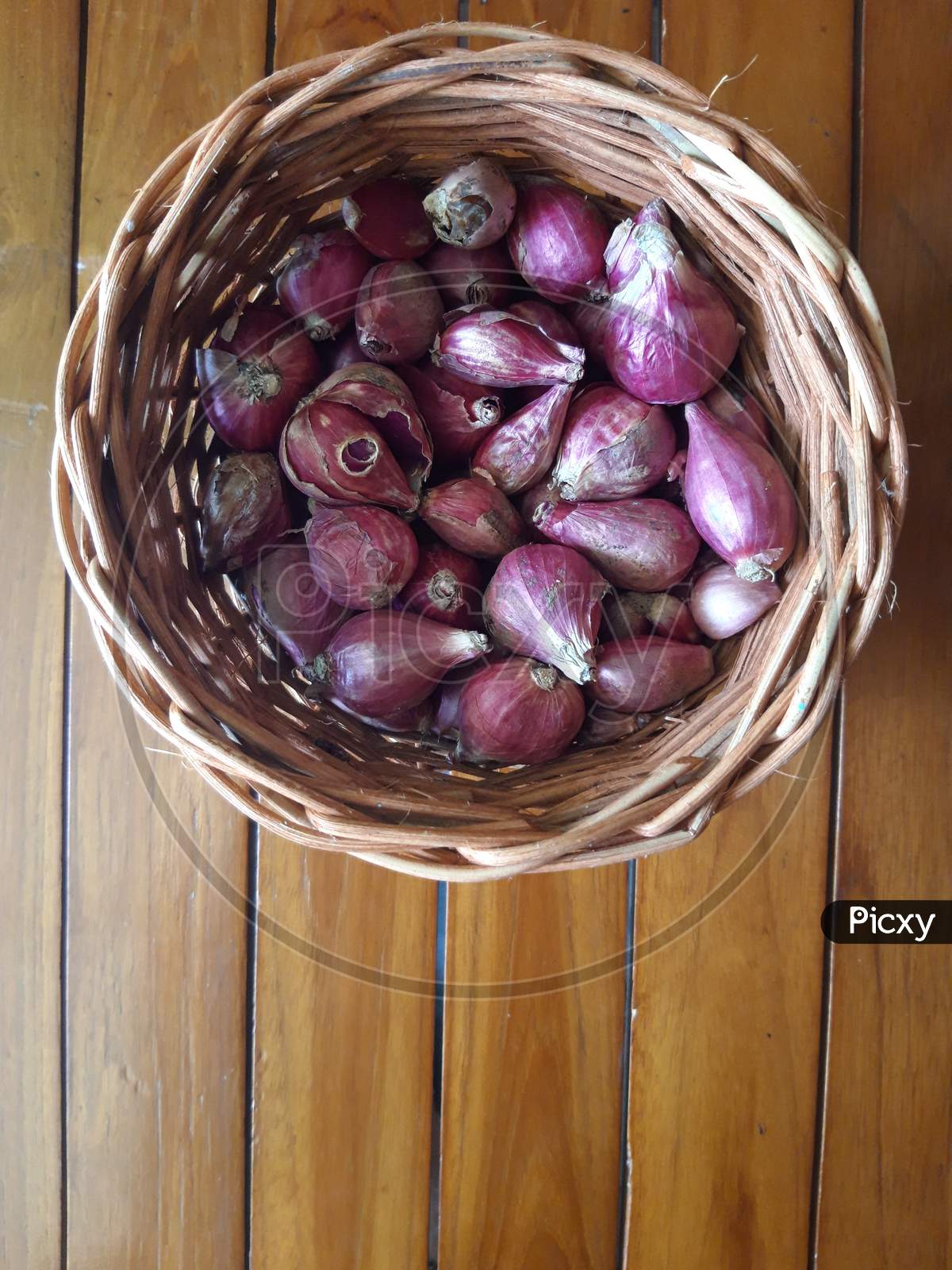 Shallots In A Wicker Basket With A Brown Wooden Base