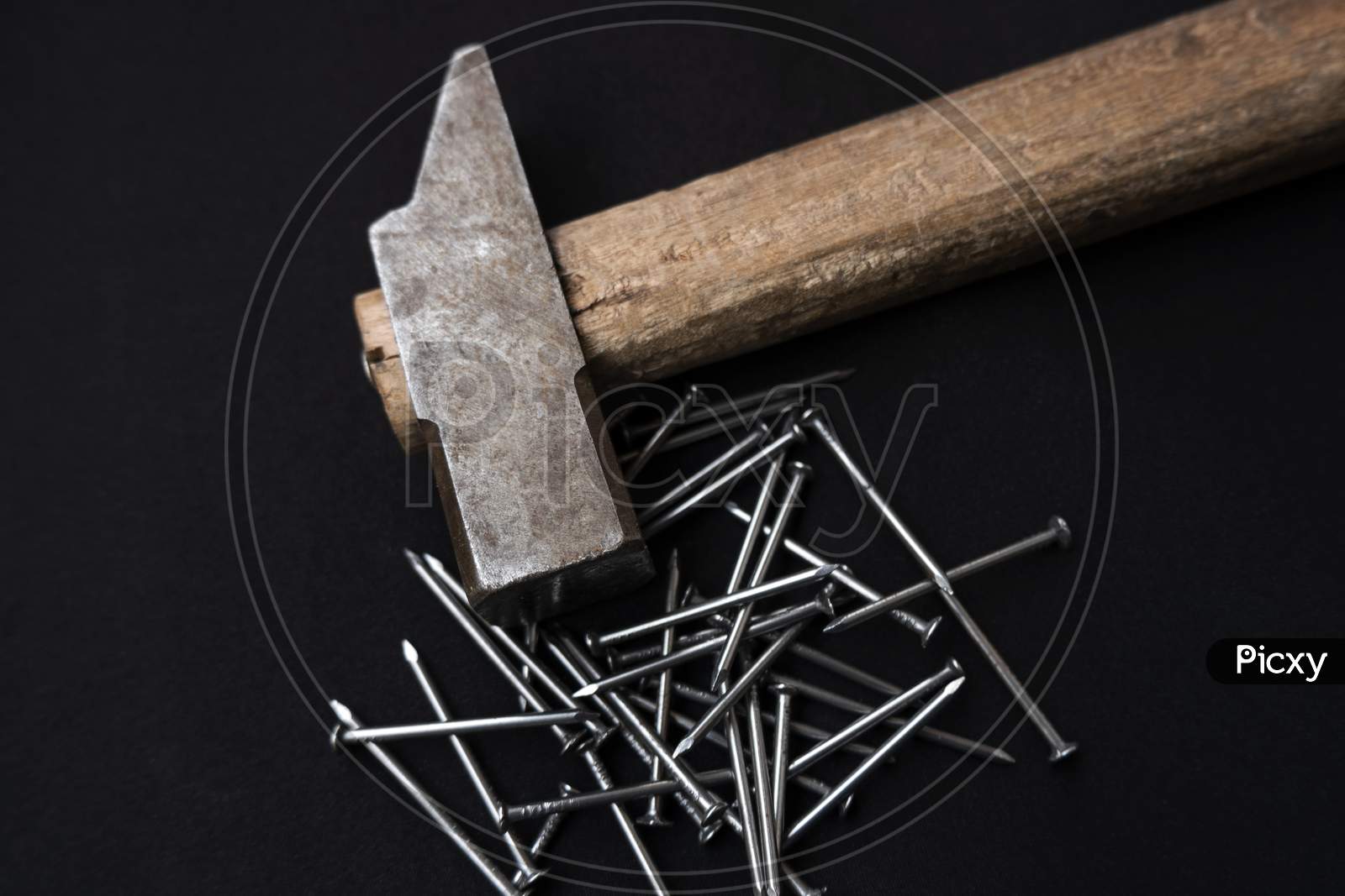 Overhead Shot Of A Pile Of Steel Nails And A Hammer With A Wooden Handle On A Black Background