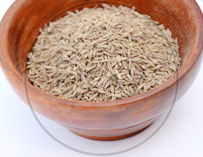 the brown cumin in the wooden bowl isolated on white background.