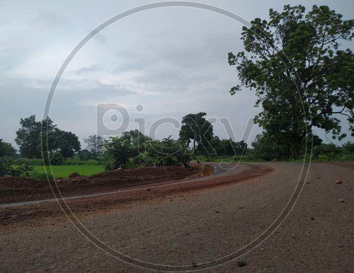 Countryside Road Between Farms Under Cloudy Sky In Monsoon