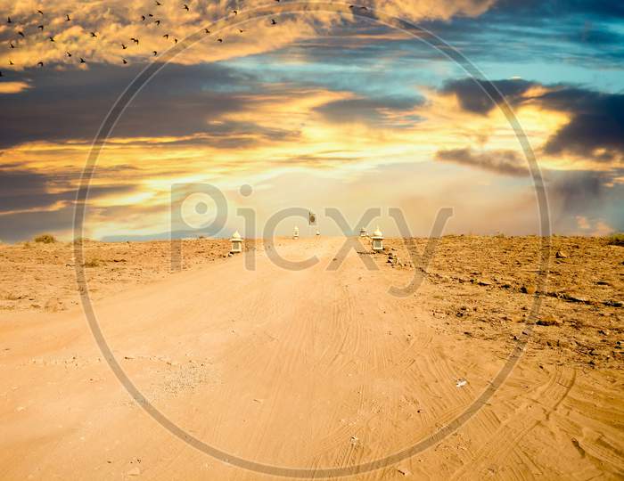 Empty Dirt Road With Barren Desert On Both Sides And Blue Sky Above Showing Thar Desert Of Rajasthan India