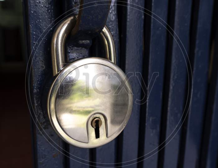 Closeup Shot Of A Shiny Padlock Handing On A Blue Metal Door Handle