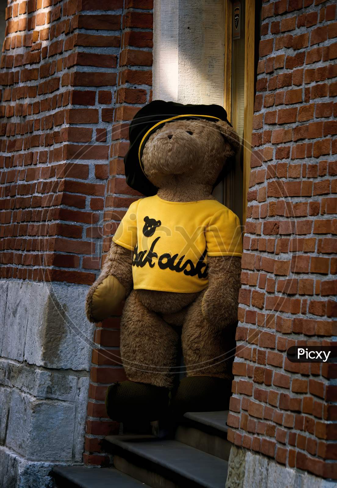 Krakow, Poland - May 03, 2015: A Huge Teddy Bear In Yellow T Shirt And A Cap Appears To Be Stepping Down From A Random Shop