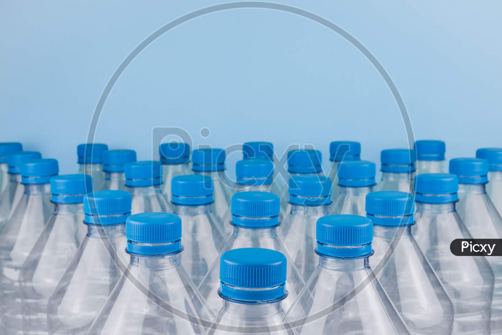 Empty Clear Plastic Bottles With Caps Stacked On A Blue Background. Recycling And Environment Concept.