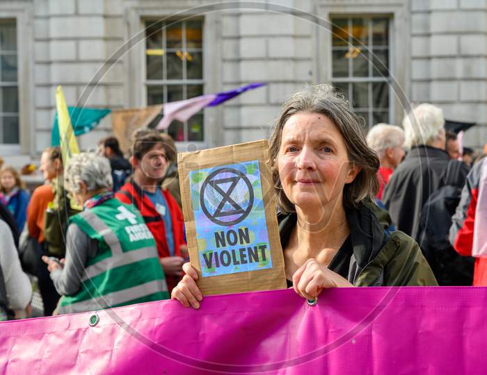 Middle Aged Female Extinction Rebellion Protester Holds A Non Violent Protest Sign And Looks At Camera