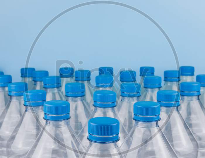 Empty Clear Plastic Bottles With Caps Stacked On A Blue Background. Recycling And Environment Concept.