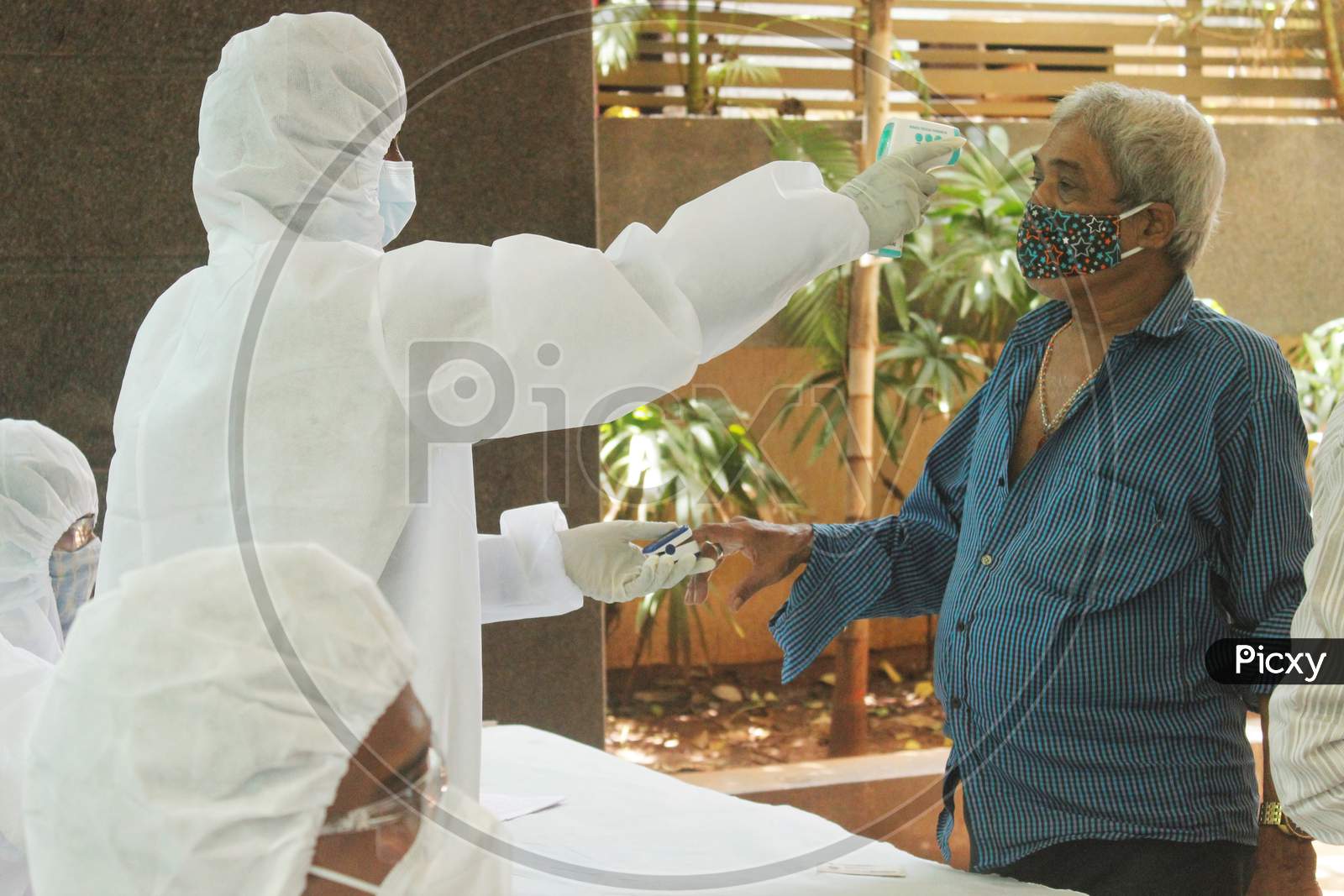 A healthcare worker wearing personal protective equipment (PPE) measures the pulse and checks the temperature of a resident of a locality during a check-up campaign for the coronavirus disease (COVID-19), in Mumbai, India on July 20, 2020.