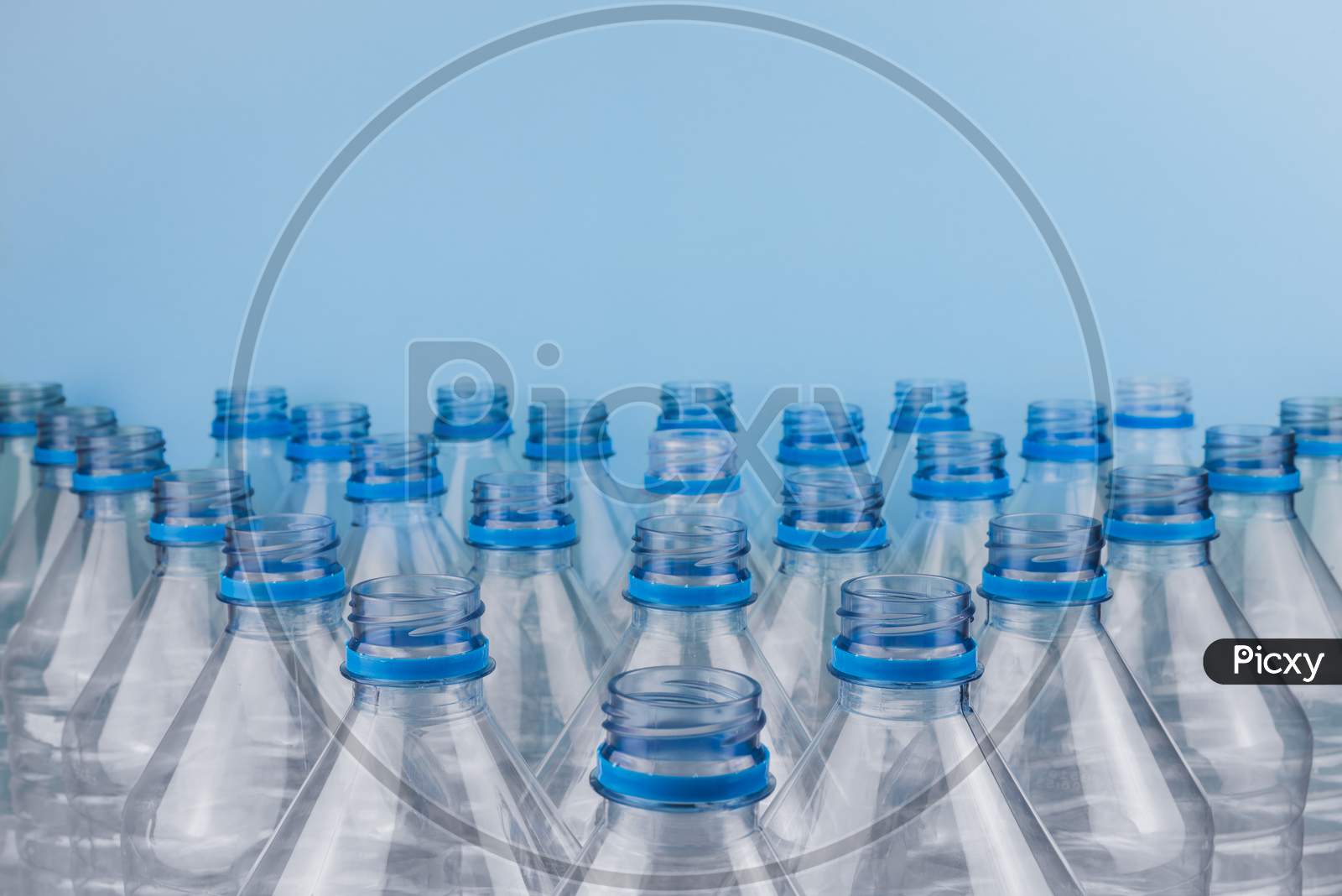 Empty Clear Plastic Bottles Without Caps Stacked On A Blue Background. Recycling And Environment Concept.