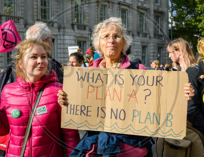 Middle Aged Female Extinction Rebellion Protester Holds A What Is Your Plan Sign And Looks At Camera