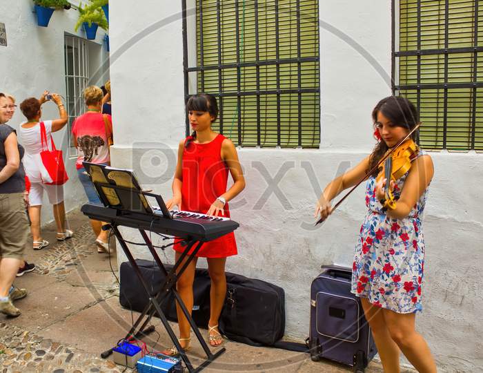 Cordoba, Spain - September 02, 2015: Two Young Girls Playing Piano And Violin As Street Performer Musician In City Center Main Square, This Is One Of The Main Touristic Attraction