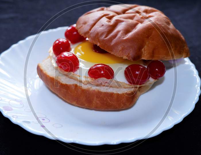 Homemade burger bun with fried egg and red cherries on a white plate . Top view image.