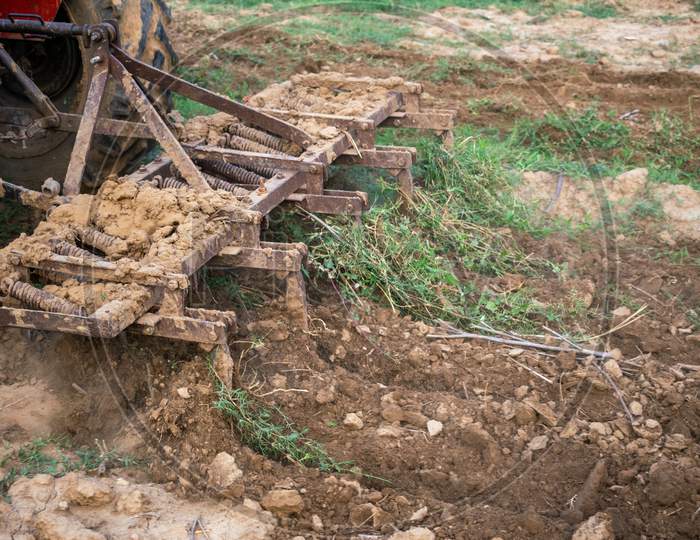 A plough of a tractor being used to plough a land for digging the soil in fields so that seeds can be planted during monsoon or rainy season in Rajasthan