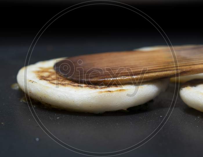 Flipping The White Utappam Dosa On Hot Non Stick Tawa With Wooden Spatula