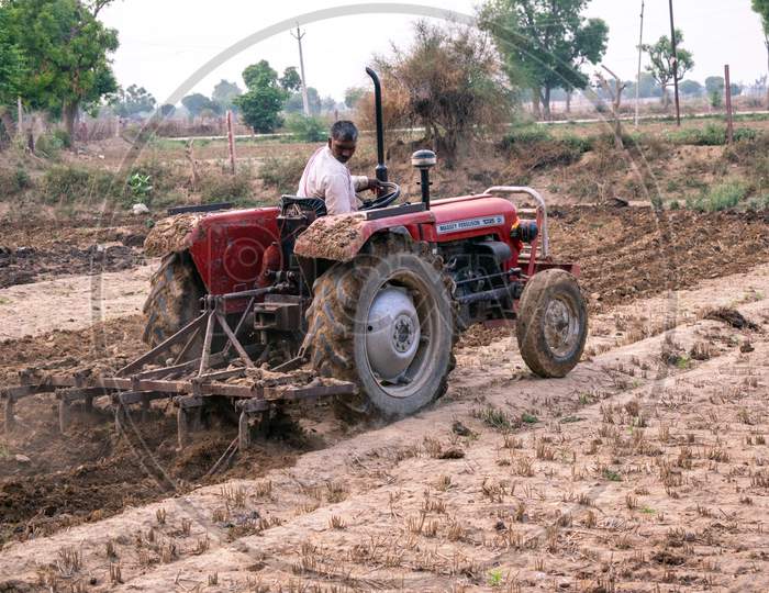 Farmers ploughing their fields using tractor to prepare it for growing kharif crops during monsoon or rainy season in Rajasthan