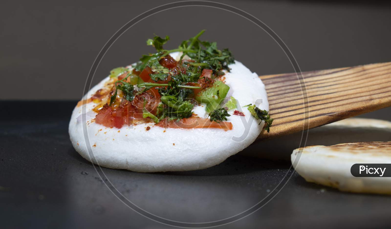 Cooking Round(Circular) White Utappam With Wooden Spatula On Hot Non Stick Pan Or Tawa