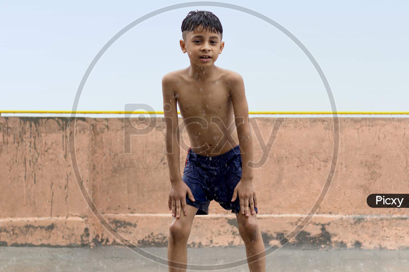 One Wet Kid Playing And Having Fun In Rain At His Terrace, Outdoors During Monsoon Season.