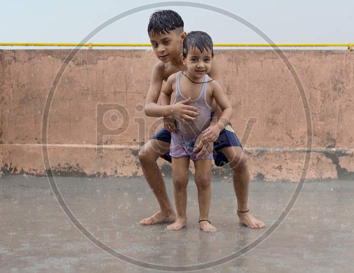 Two Wet Kids Playing And Having Fun In Rain At Their Terrace, Outdoors During Monsoon Season.