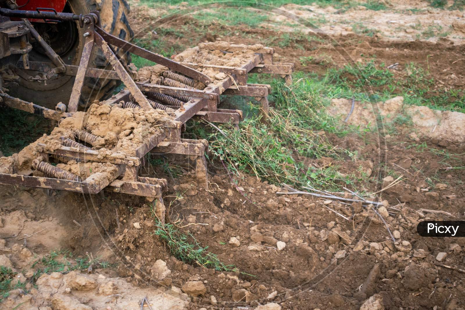 A plough of a tractor being used to plough a land for digging the soil in fields so that seeds can be planted during monsoon or rainy season in Rajasthan