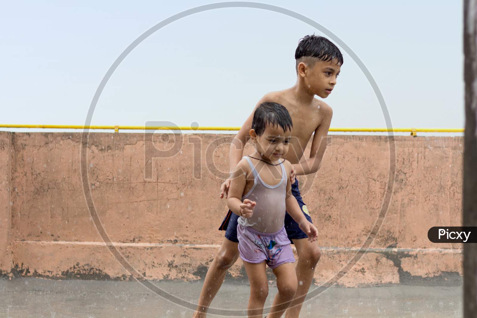 Two Cute Kids Wet, Playing And Having Fun In Rain At Their Terrace, Outdoors During Monsoon Season.