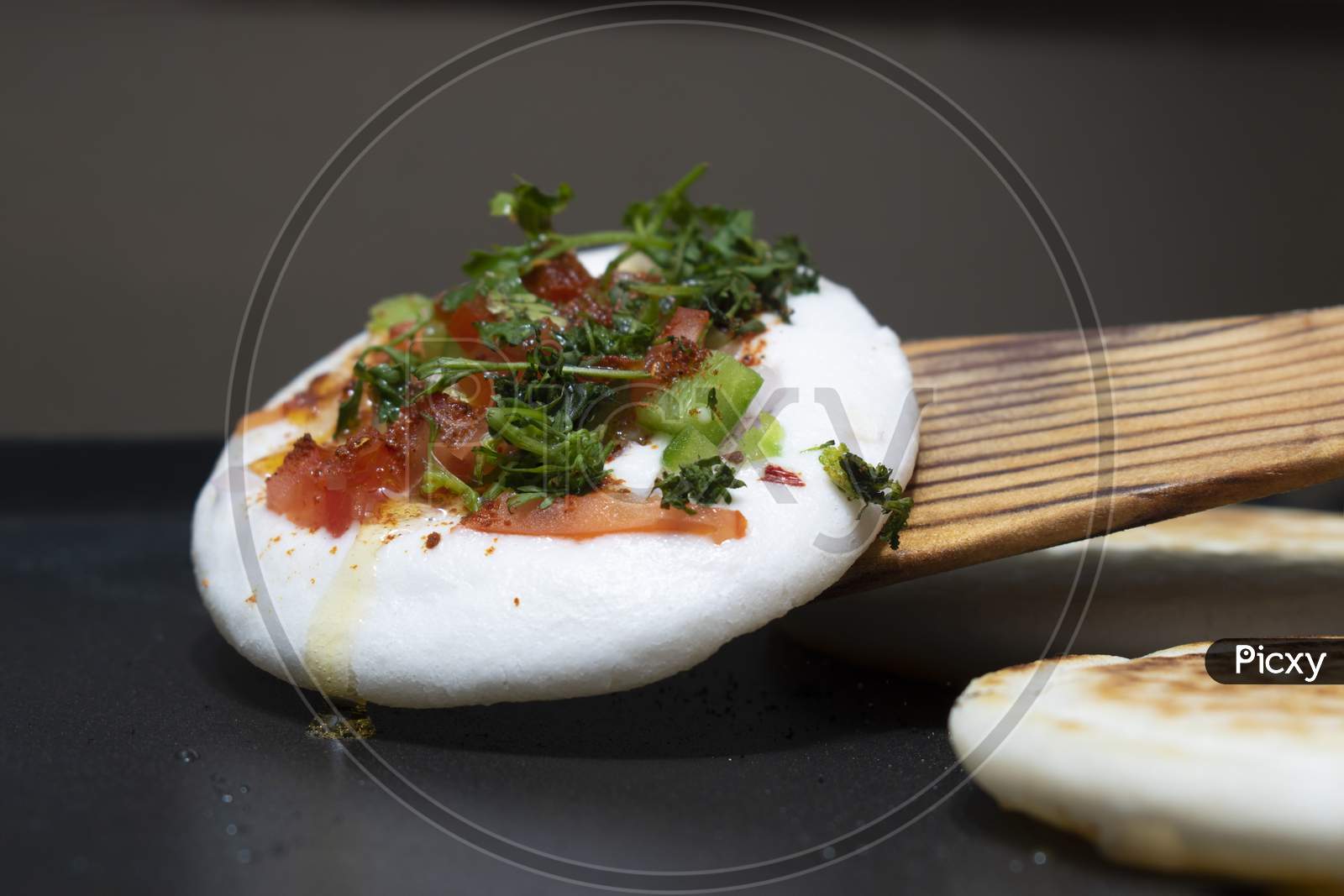 Cooking (Circular) White Utappam With Wooden Spatula On Hot Non Stick Pan Or Tawa