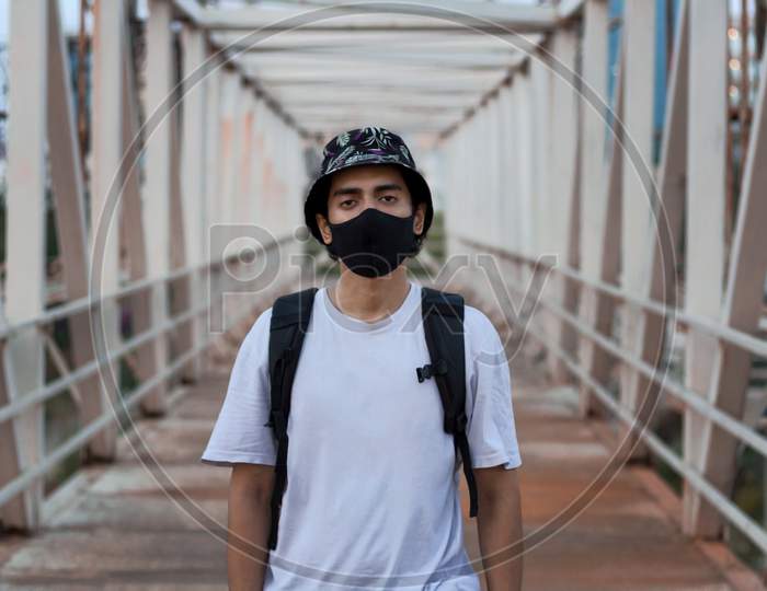 Portrait Of A Young Millennial Standing On An Empty Metal Foot Bridge Outdoors While Wearing A Black Protective Face Mask To Prevent Covid-19 Virus Infection In A City. The New Normal.