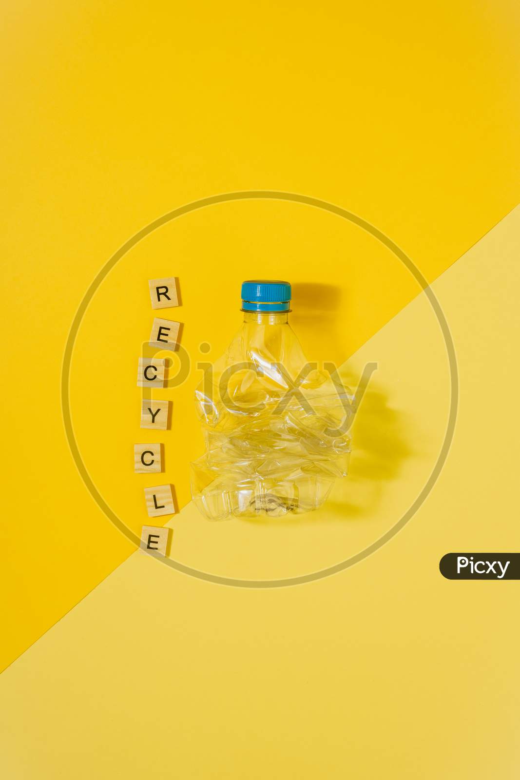 Transparent And Crushed Plastic Bottle With Blue Cap On A Yellow Background And The Word Recycle. Recycling And Environment Concept.