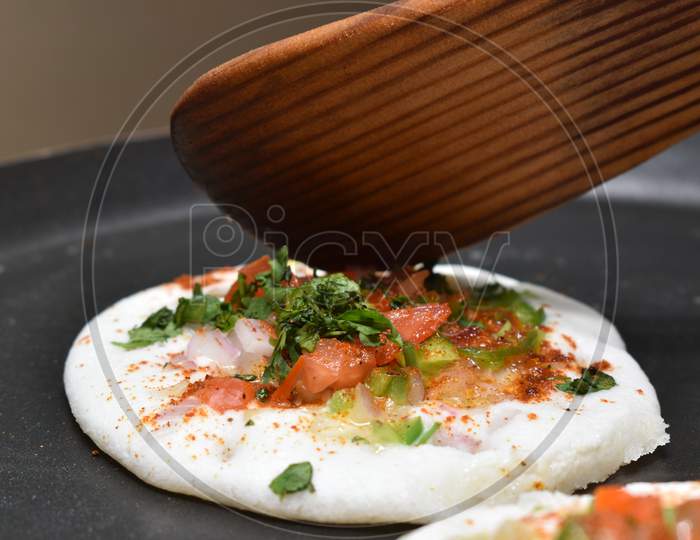 Cooking Mini Onion White Utappam With Wooden Spatula On Hot Non Stick Pan