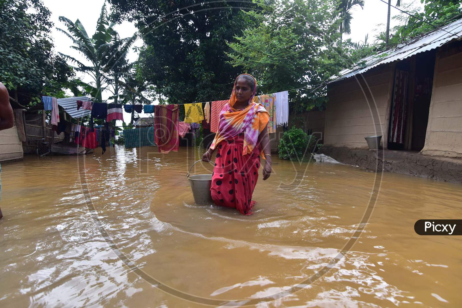 A woman carries a bucket of drinking water while she wades her way through the floodwaters in a flood-affected village in Nagaon, Assam on July 22, 2020