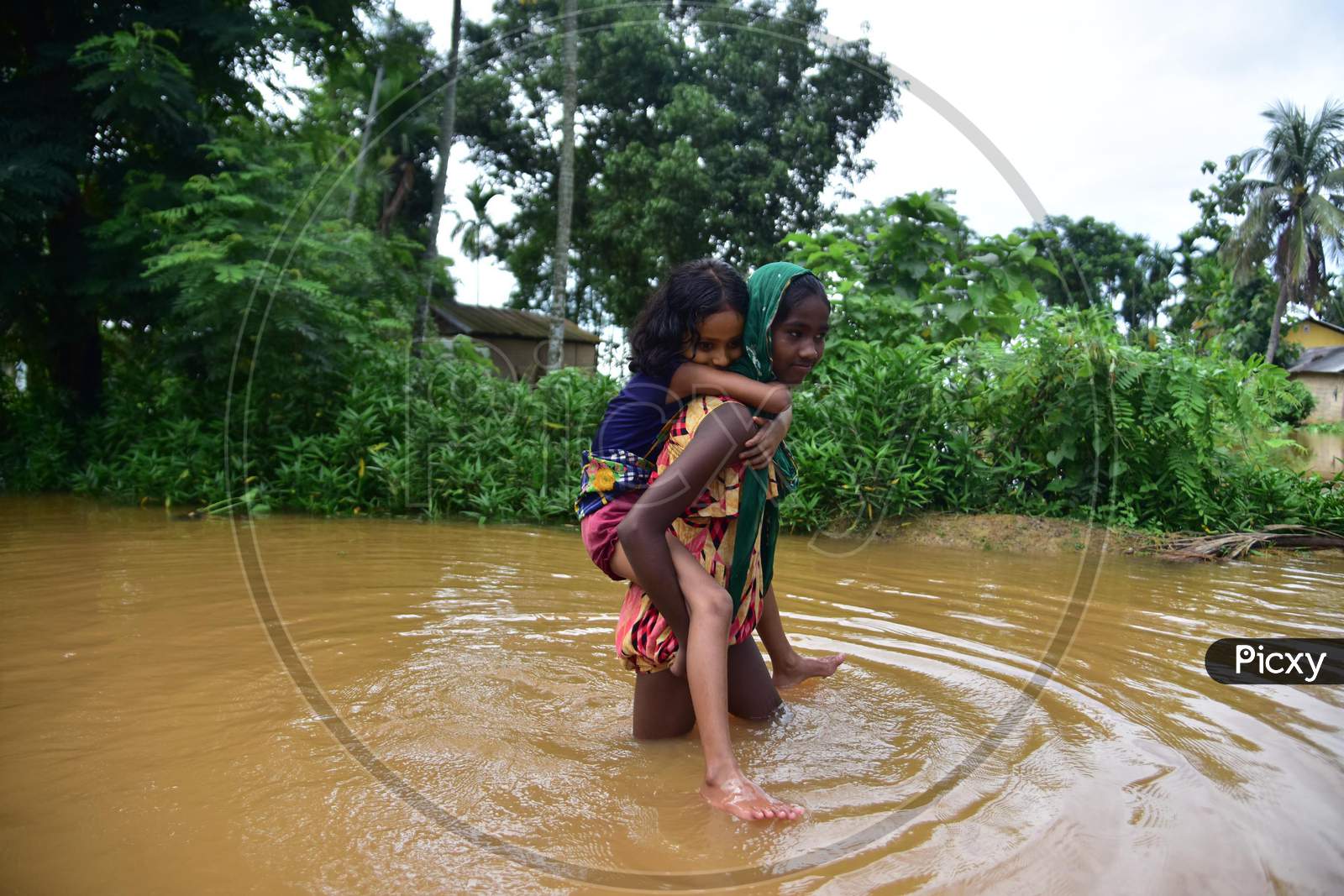A girl carries another girl on her back as she wades through the floodwaters in the flood-affected village in Nagaon, Asam on July 22, 2020