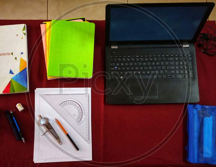 An Organized Table With A Laptop,Earphones,Bottle,Books,Pen,Geometrical Instruments And A Pen Pouch.