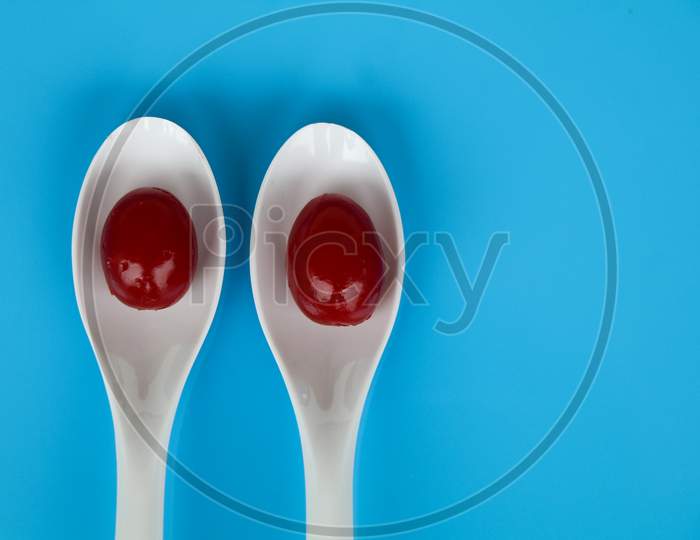 Red Color Cherry Fruits In A White Spoon Against Light Blue Background, With Copy Space, Caption