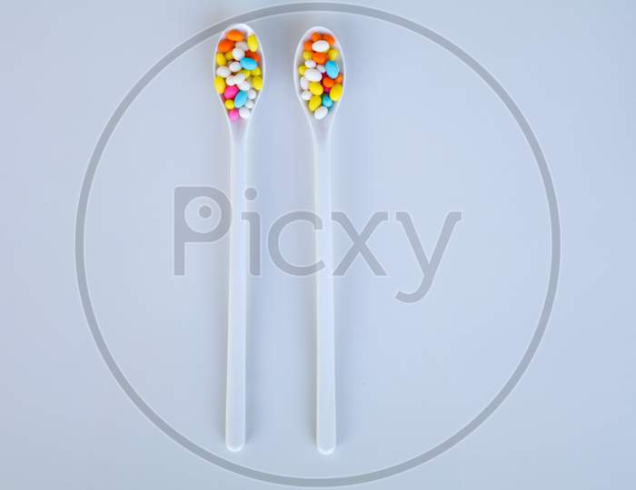 Multi Colored Fennel Sugar Candy In White Spoons Against White Background With Copy Space, Isolated