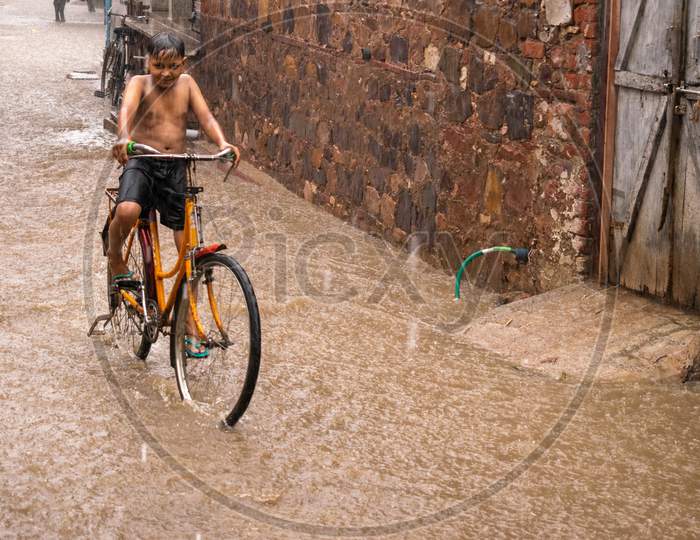 A boy rides bicycle in waterlogged streets and takes bath when it rains during monsoon in Bharatpur