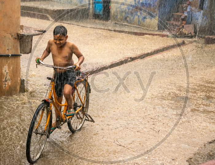 A boy riding bicycle and having fun in rain during monsoon in Bharatpur
