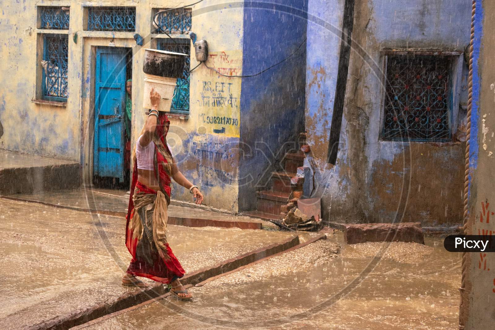 A woman carries pots on head on a road while it rains heavily during monsoon season in Bharatpur